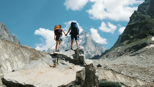 Couple of Tourists with Backpacks in the Campaign Raise Their Hands Up on the Top of the Mountains alt