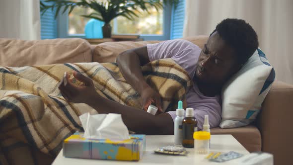 Sick African Man in Blanket Measuring Temperature with Infrared Scanner at Home alt