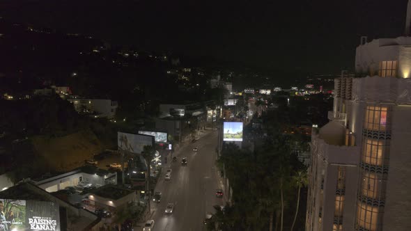 Cinematic drone flies around a skyscraper revealing a major boulevard in Los Angeles at night alt