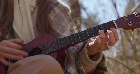 girl's hands play the ukulele at sunset in the forest. close-up alt