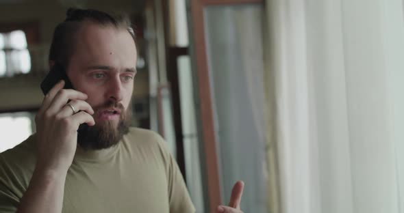 Handsome Man Shouting Emotionally on a Mobile Phone and Looking Out Window alt