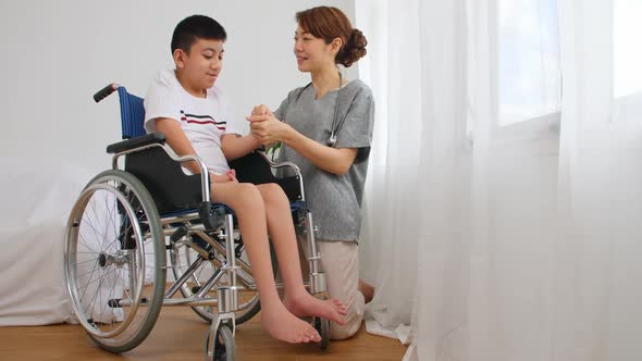 A physical therapist is talking to a disabled boy in a wheelchair. alt