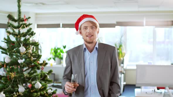 Handsome Young Blond Businessman Wearing Christmas Hat Holding Glass of Wine Smiling Coming Forward alt