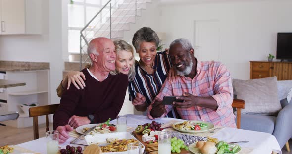 Diverse senior couples sitting by a table drinking wine eating dinner and taking a selfie alt