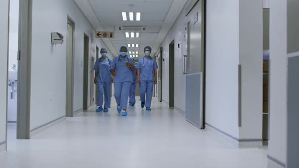 Diverse female doctors wearing face masks walking in hospital corridor alt