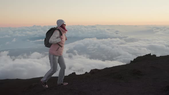 Happy Woman with Backpack Hiking Up Scenic Volcanic Mountain Peak at Pink Sunset alt