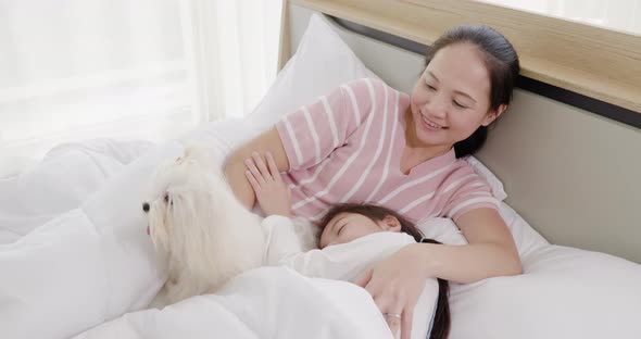 Mother and daughter playing with white dog on bed 3