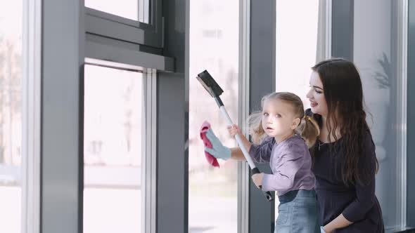 Toddler Girl Is Cleaning the Windows with a Mop with Her Mother alt