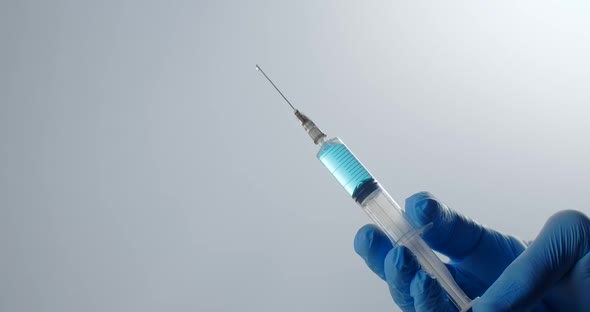 The Nurse is Holding a Full Syringe with a Long Needle Drop of Medication Drips From the Needle of