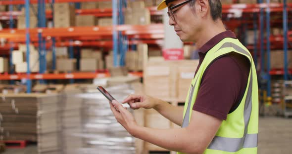Asian male worker wearing safety suit and using smartphone in warehouse alt