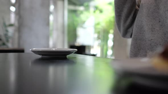 Closeup of a woman drinking and putting a cup of hot coffee down on a saucer