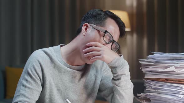 Close Up Of Tired Asian Man Yawning While Working Hard With Documents At Home alt