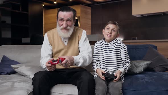 Granddad which Playing Video Game with His 13-Aged Cheerful Grandson Using Gamepads alt