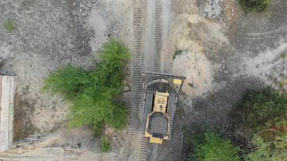 Top Aerial View on Tracked Bulldozer Rides on Sandy Road at Construction Site alt