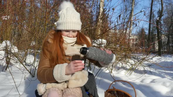 Red-Haired Teen Girl Sitting In Snowy Park And Having A Snack. Girl Laughing