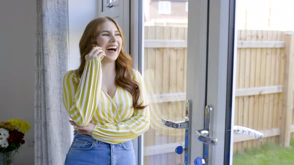 Smiling woman leaning on glass door, talking on the phone
