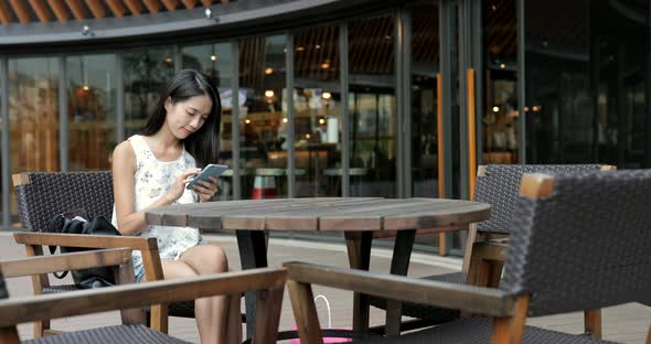 Woman using mobile phone and sitting at outdoor coffee shop alt