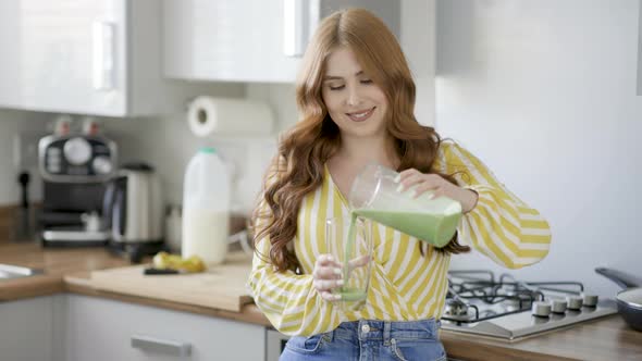 Young woman in kitchen pouring green smoothie in glass