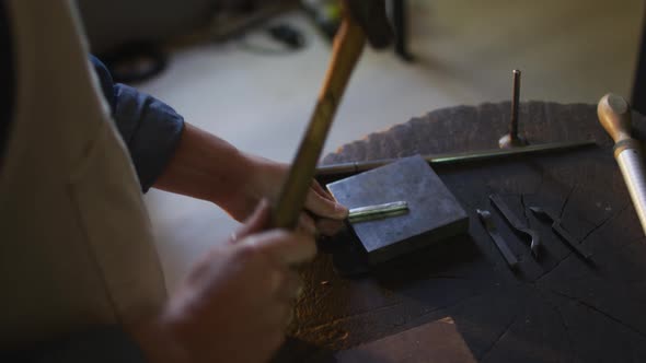 Close up of hands of caucasian female jeweller using hammer, making jewelry alt