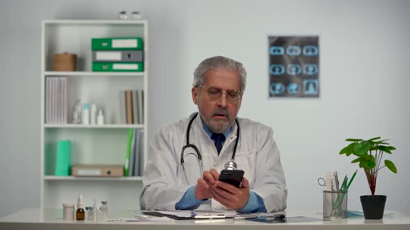 Male Doctor Fills Out Medical History and Advises Patient Using Mobile Phone About Treatment alt