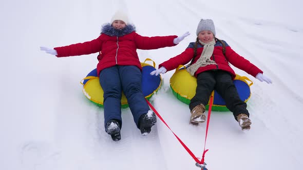 Children in Winter Ride in Snow on an Inflatable Snow Tube and Play Superheroes alt