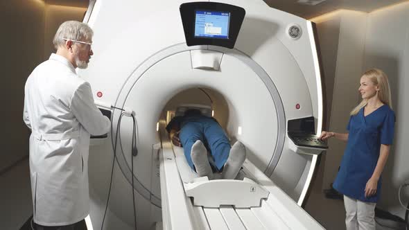 In Medical Laboratory Senior Radiologist Controls MRI or CT or PET Scan with Male Patient Undergoing