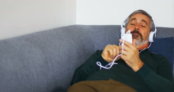 Man listening to music on mobile phone while lying on sofa 4k alt