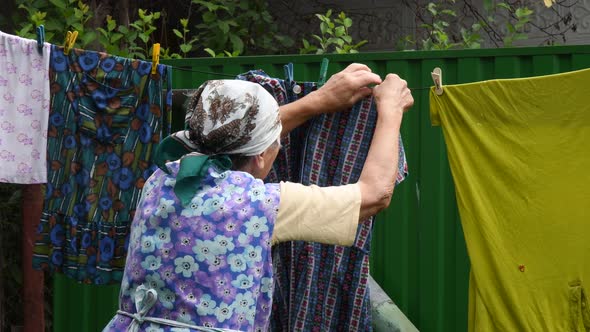 Rural old woman hanging laundry on clothepins outdoor