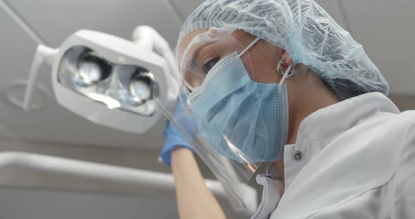 Dentist Holding Hand on Special Lamp Looking at Client in Chair alt