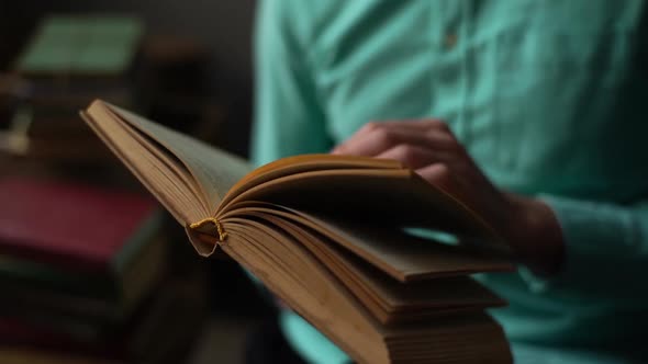 Closeup Hands of Unrecognizable Young Man Flipping Through Pages of Old Frayed Book Sitting in Chair alt