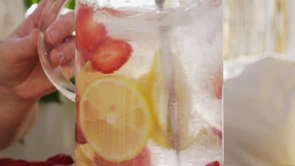 Woman Mixes Drink with Lemon and Strawberry Slices in Jug