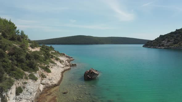 Aerial shot of a small beach with a rusted ship wreck in the foreground. Drone flies over the wreck. alt