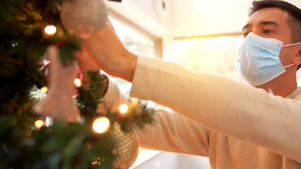 Man in Mask Decorating Christmas Tree at Home alt