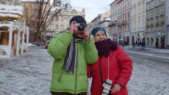 Senior Wife Husband Tourists Taking Photo Pictures on Retro Camera Walking on Winter City Street alt