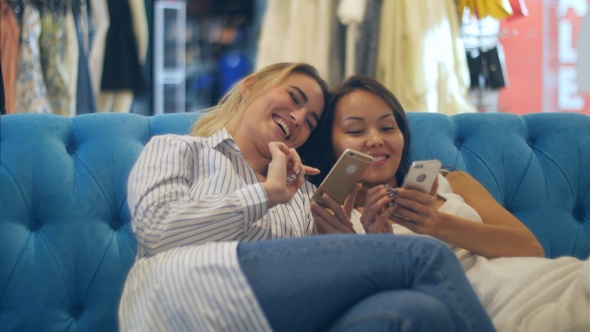 Happy shopping women use smartphone and laugh sitting in mall