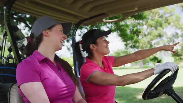 Two caucasian women playing golf riding a golf cart talking and laughing alt