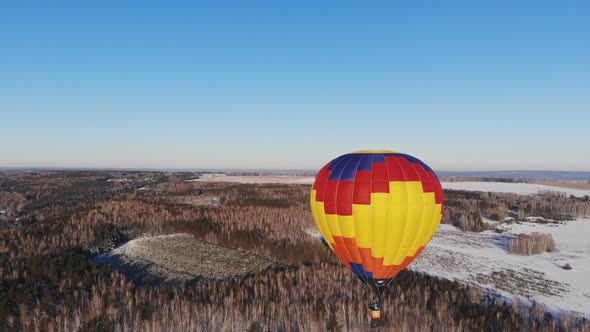 Aerial Shot of the People Fly on a Big Bright Balloon Over the Winter Forest