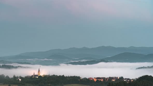 Fog Coming Down from Mountain Range to Village at Sunset