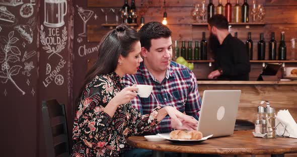 Caucasian Couple Looking at Laptop and Drinking Coffee with Croissants alt