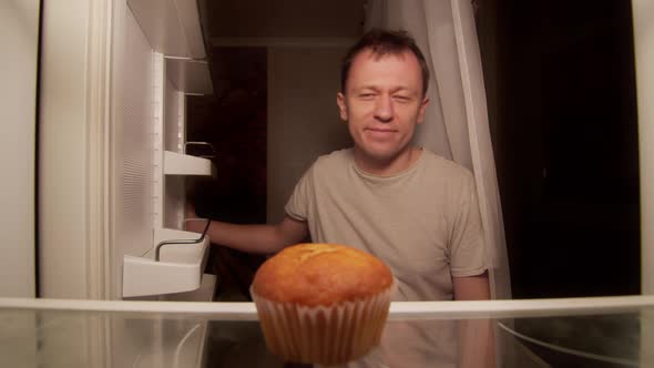 A man opens the refrigerator at night on the shelf is one cupcake, a disgruntled man alt