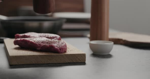 Slow Motion Orbit Shot of Man Grinding Pepper on Raw Beef Steak on Oak Board alt