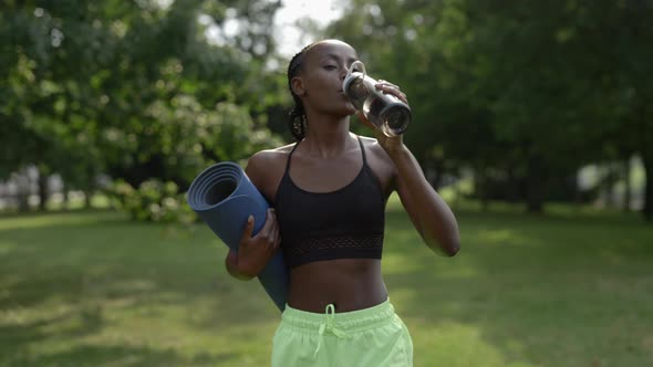 Woman in Sportswear Drinking Water and Carrying Yoga Mat alt