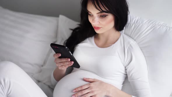 Pregnant Attractive Woman Using Mobile Phone At Bed alt