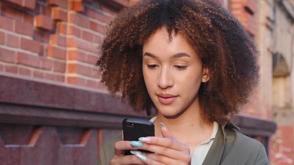 Young African American Woman Using Smartphone Surfing Social Media Checking News or Texting Messages alt