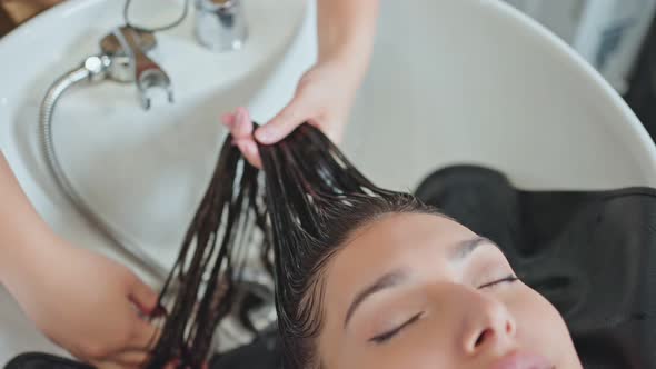 Caucasian young woman lying down and close eye on salon washing bed getting hair washed in salon. alt