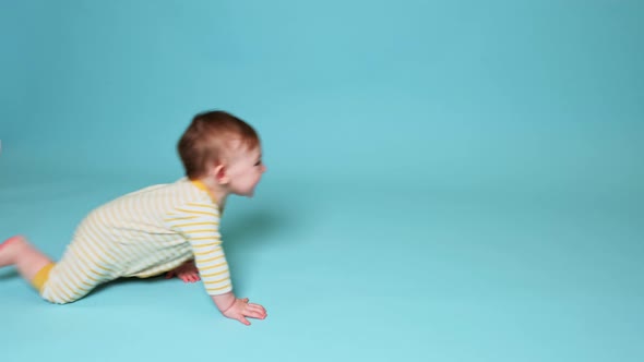 Happy toddler baby boy crawls on studio blue background. Smiling baby crawling fast on the floor