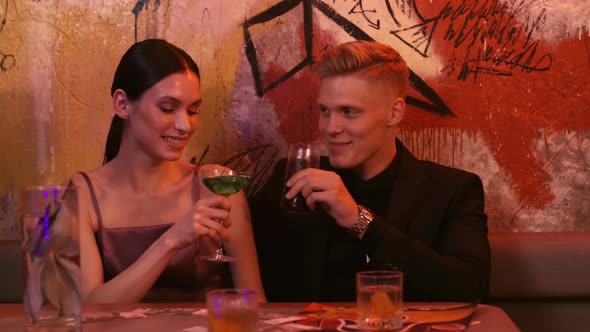 A Man and a Woman on a Date in a Restaurant Clink Glasses of Cocktails