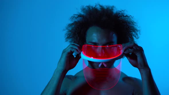 Man wearing light therapy mask against blue wall alt