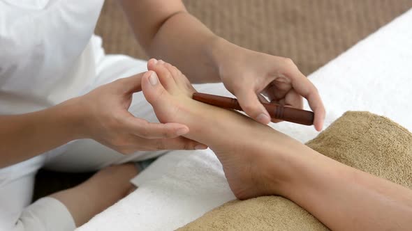Professional therapist giving traditional thai foot massage with stick to a woman in spa
