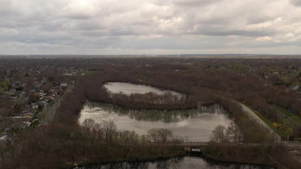 A drone view high over a quiet lake, surrounded by dry, brown trees on a cloudy day. The cloudy skie alt